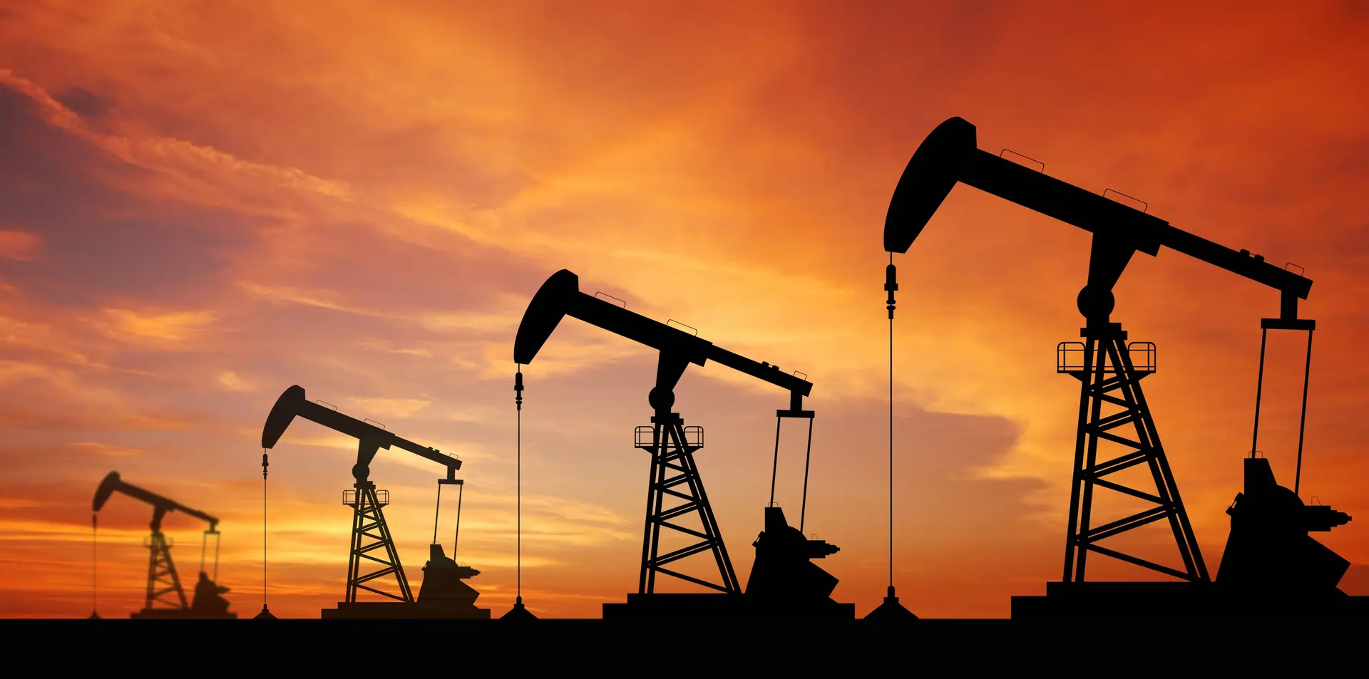 Oil field pump jacks silhouetted against a sunset sky.